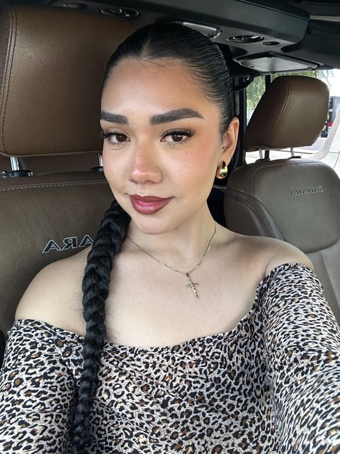 Woman with black braided hair wearing a leopard print off-shoulder top, taking a selfie inside a car